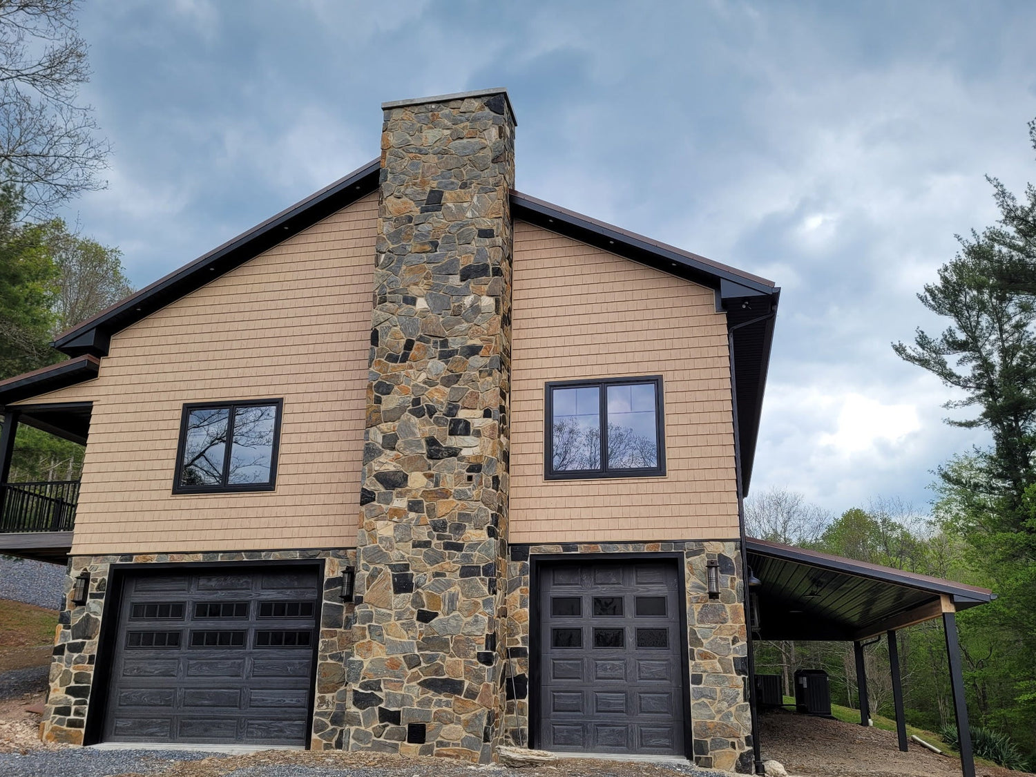 Two-story house with stone chimney and garage doors, surrounded by trees.